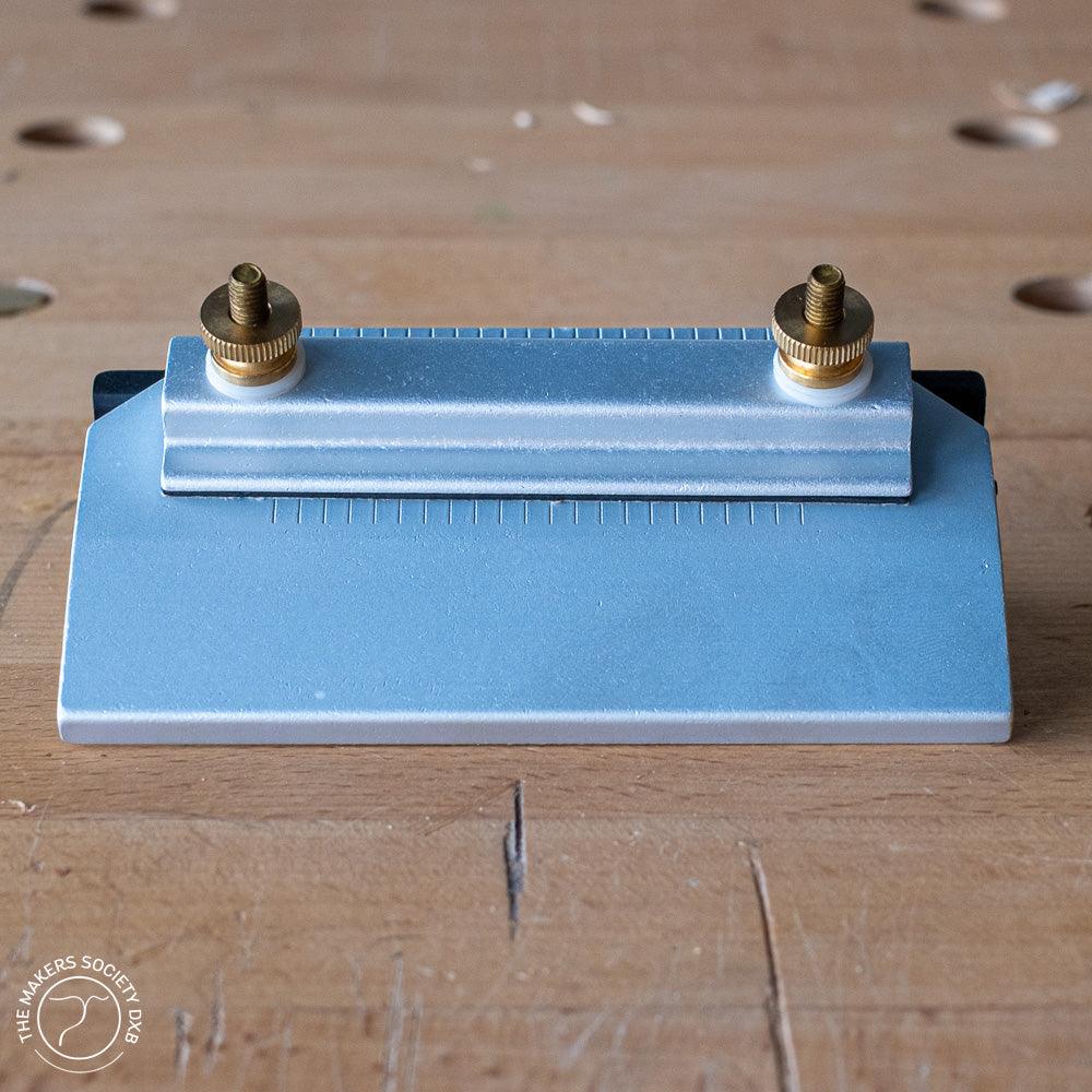 Narex metal honing guide for woodworking placed on a wooden workbench with brass adjustment screws