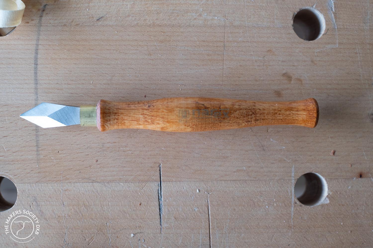 Marking knife with wooden handle and sharp steel blade on woodwork bench surface