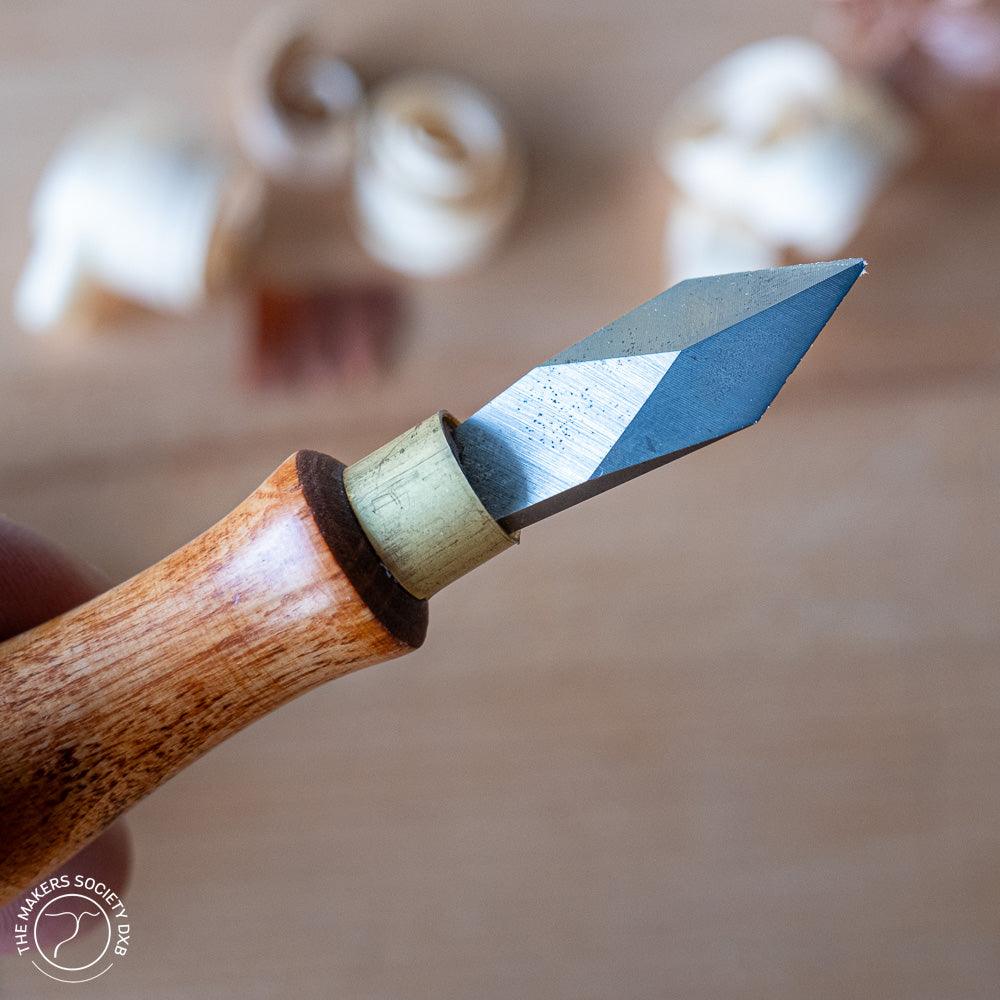 Close-up of a Narex marking knife with wooden handle and sharp angled blade on blurred woodwork background