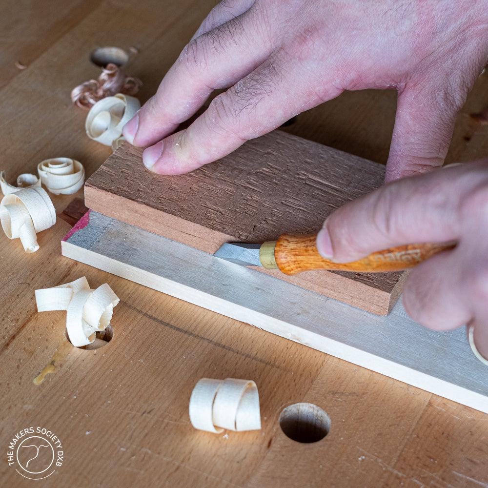 Hand using Narex marking knife with wooden handle to cut wood piece on workbench with wood shavings
