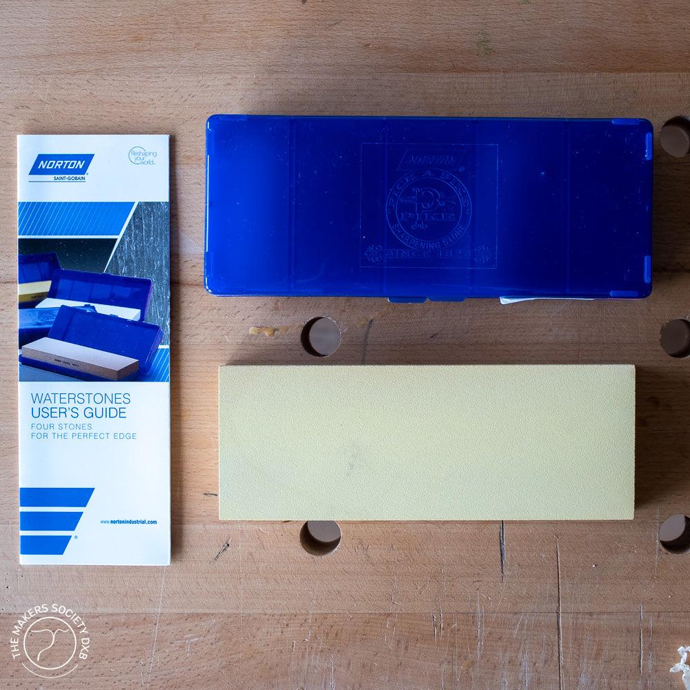 Norton Waterstone sharpening stone with blue plastic case and user's guide on a wooden workbench