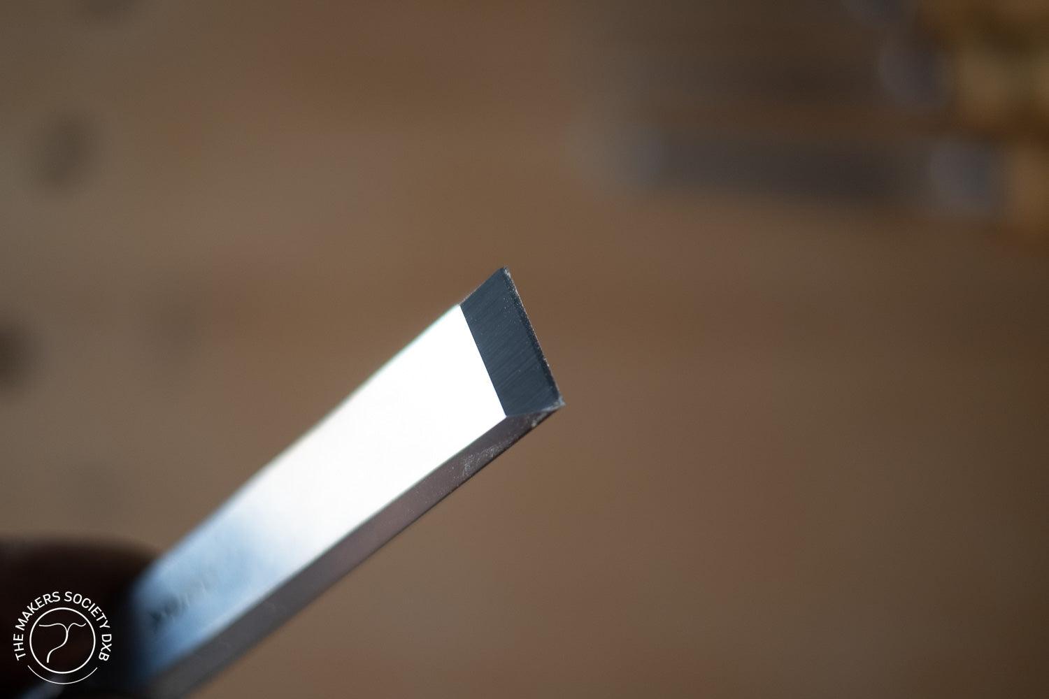 Close-up of a sharp bevel edge chisel blade for woodworking with blurred wooden background