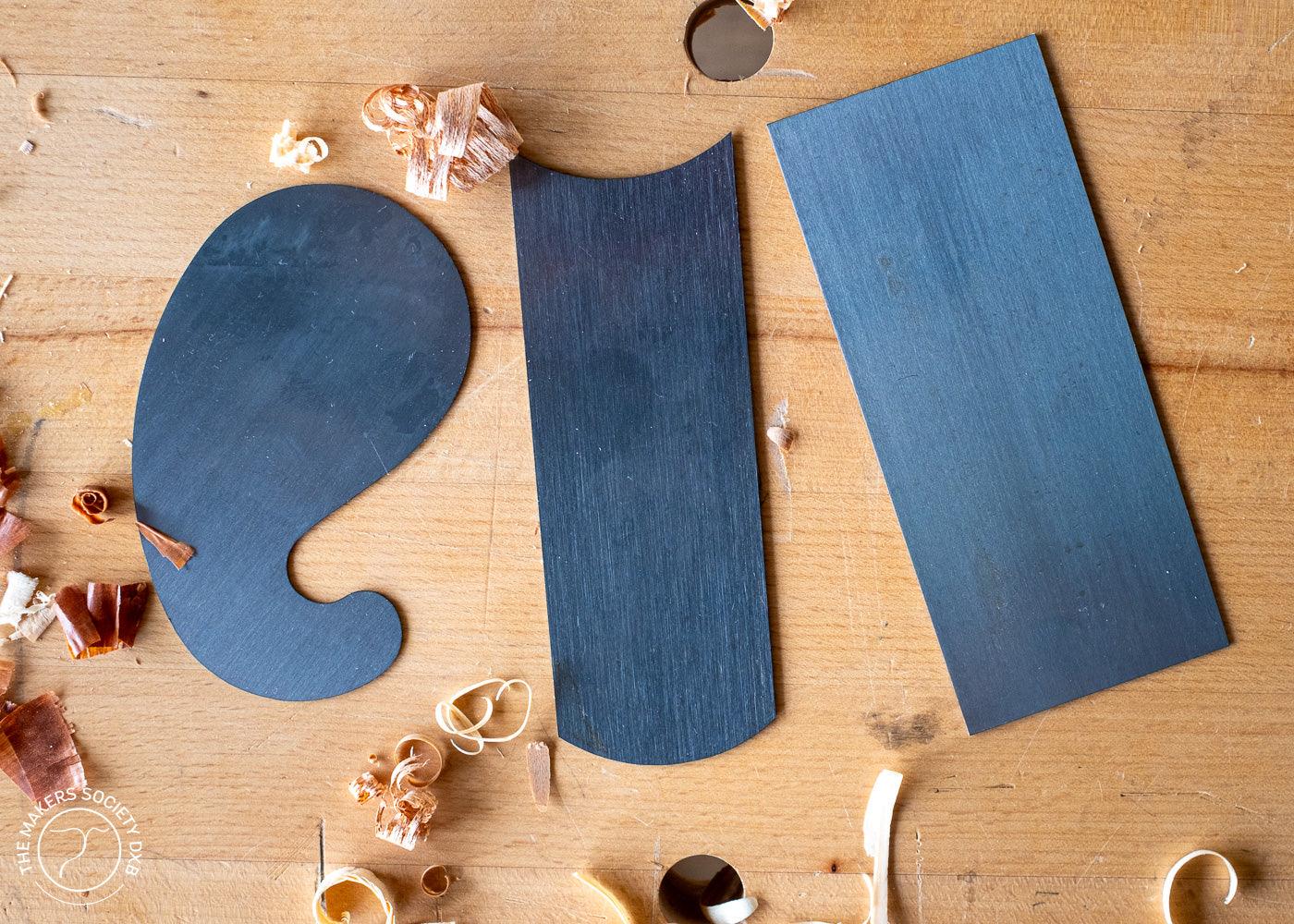 Set of three premium black cabinet scrapers on a wooden surface with wood shavings