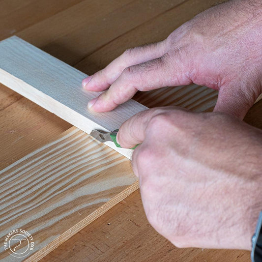 Hands using a marking knife on a wooden board for precise woodworking in a maker workshop