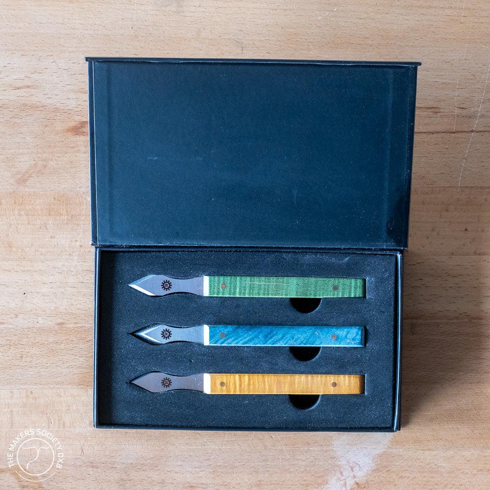 Set of three Richter marking knives with green, blue, and yellow wooden handles in black foam box on wooden surface