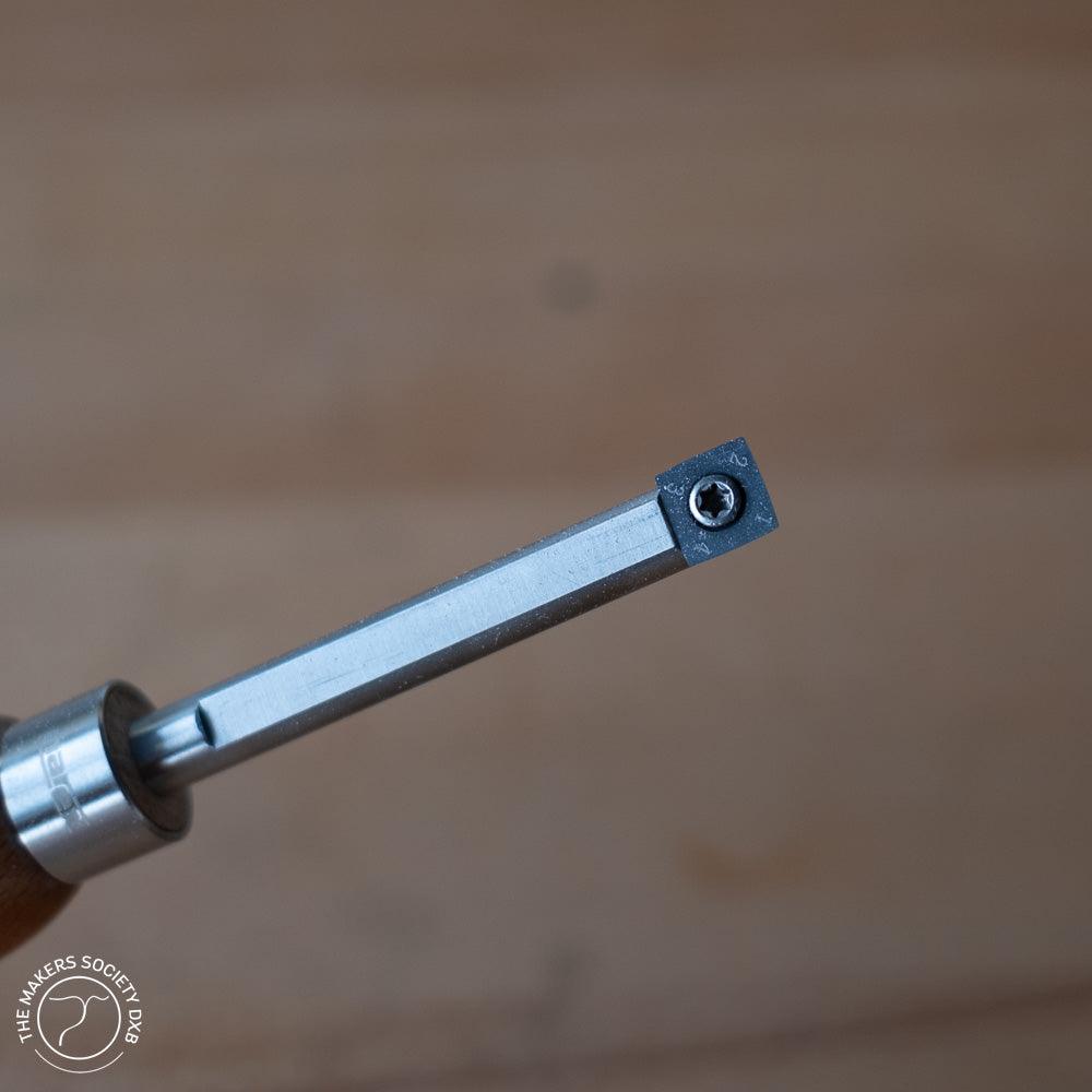 Close-up of a Narex turning tool with carbide tip and wooden handle on a blurred wood background