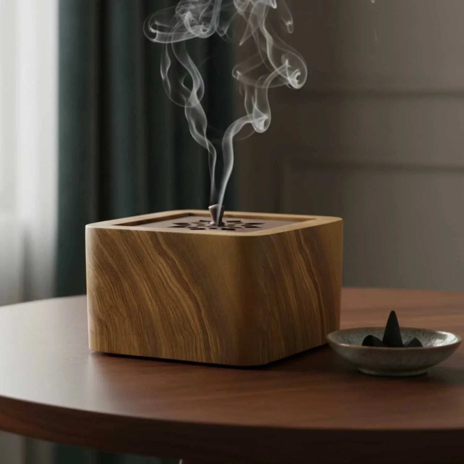 Wooden square incense burner on round table with smoke rising, ceramic dish with cones nearby
