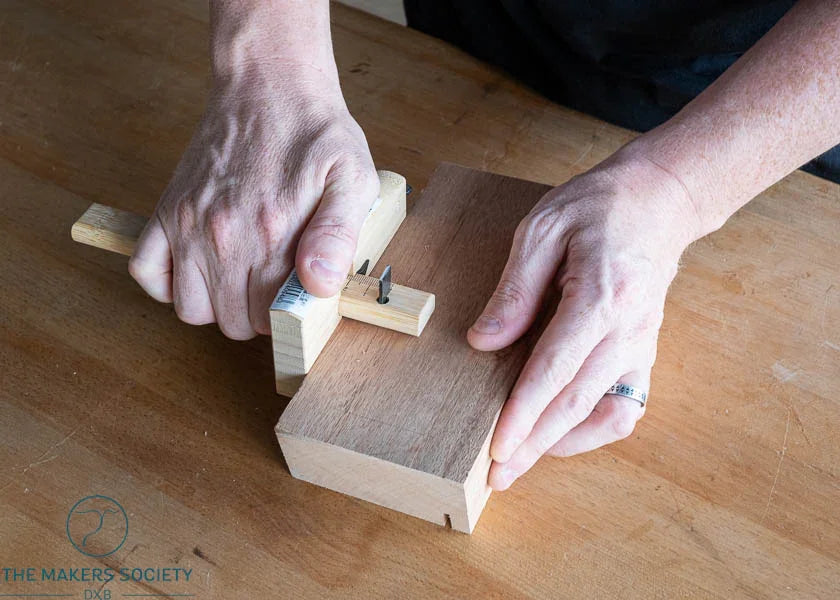 Hands using Kakuri marking gauge with 120mm blade to mark wood on a workshop table