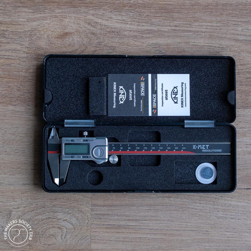 K-MET Absolute Zero digital caliper in black foam case with certification cards on wooden surface