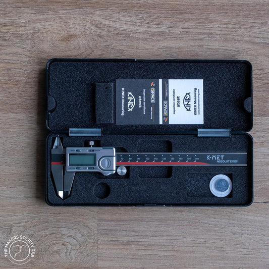 K-MET Absolute Zero digital caliper in black foam case with certification cards on wooden surface