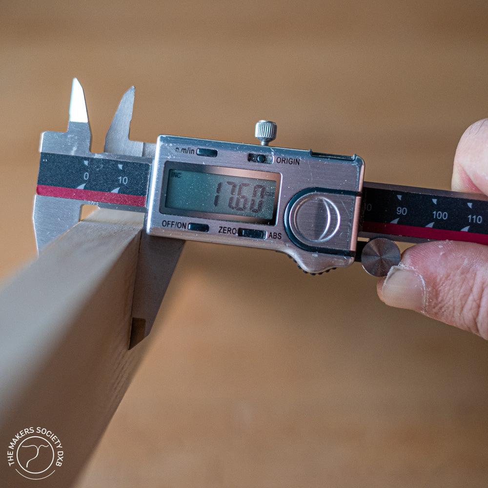 Digital caliper measuring a wooden plank with a precise 17.60mm reading, held by hand