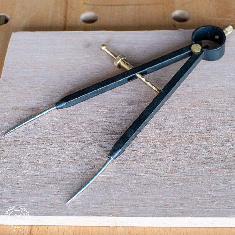 Black spring bow divider with brass adjustment screws placed on wooden board in woodworking workshop