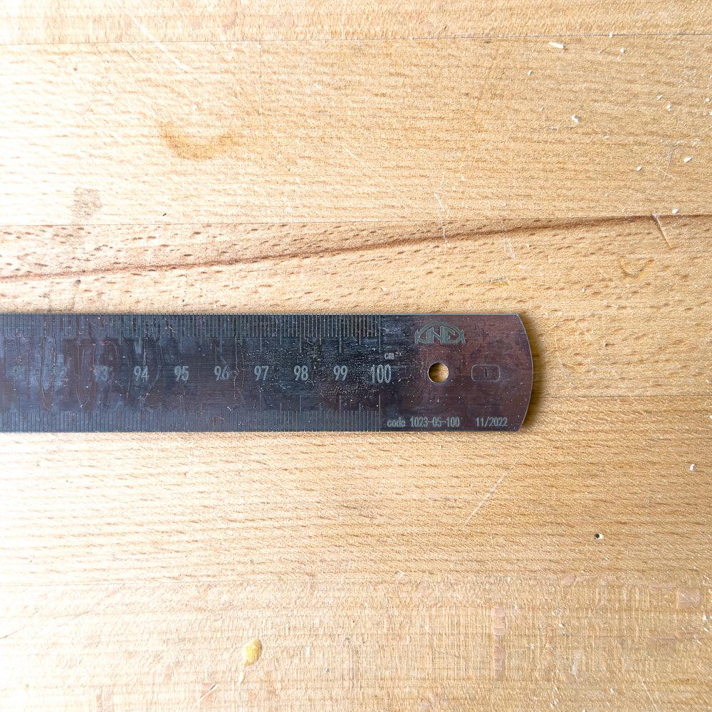 Close-up of a black metal steel ruler marked up to 100 centimeters on a wooden surface