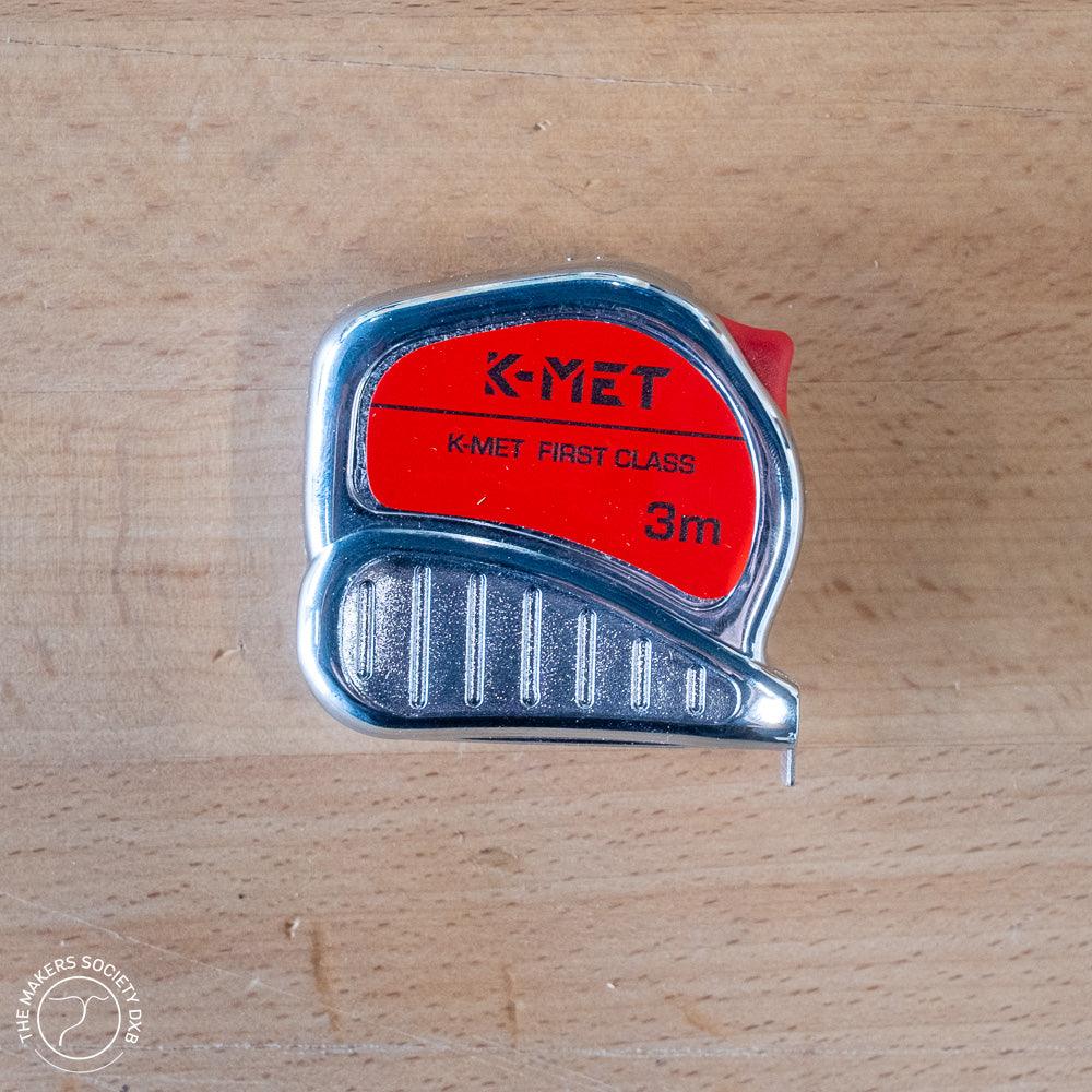K-MET First Class 3m tape measure with red and chrome casing on wooden surface
