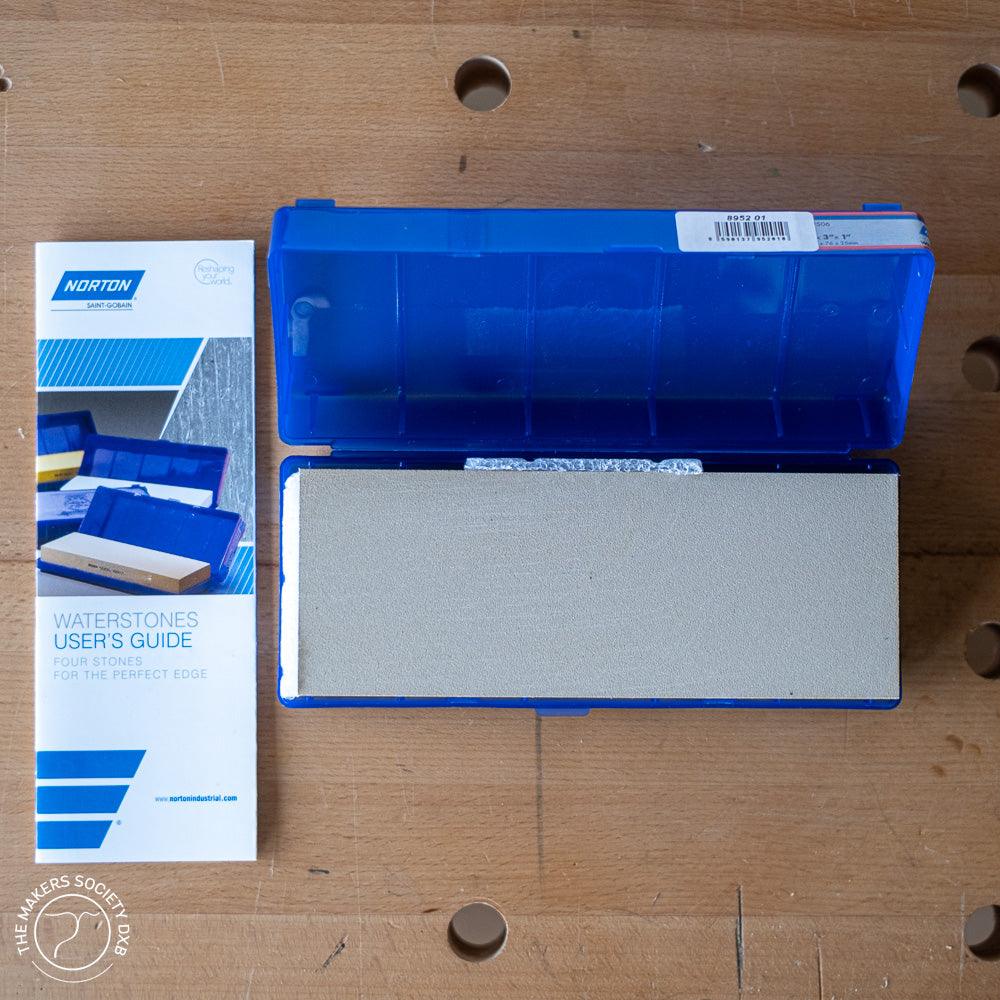 Norton 1000 grit waterstone in blue plastic case with user’s guide on wooden workbench