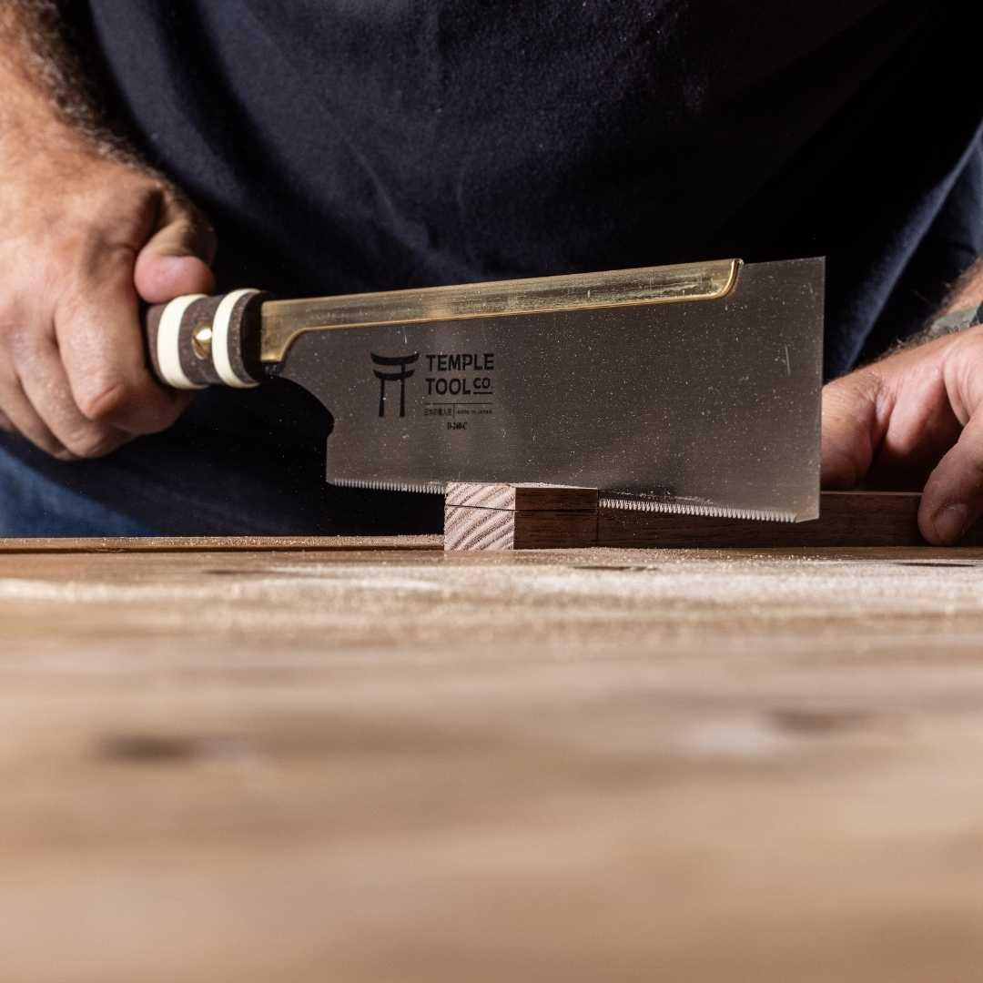 Close-up of hands using a Temple Tool Co. 240mm dozukis pull saw cutting fine woodworking joint on wood