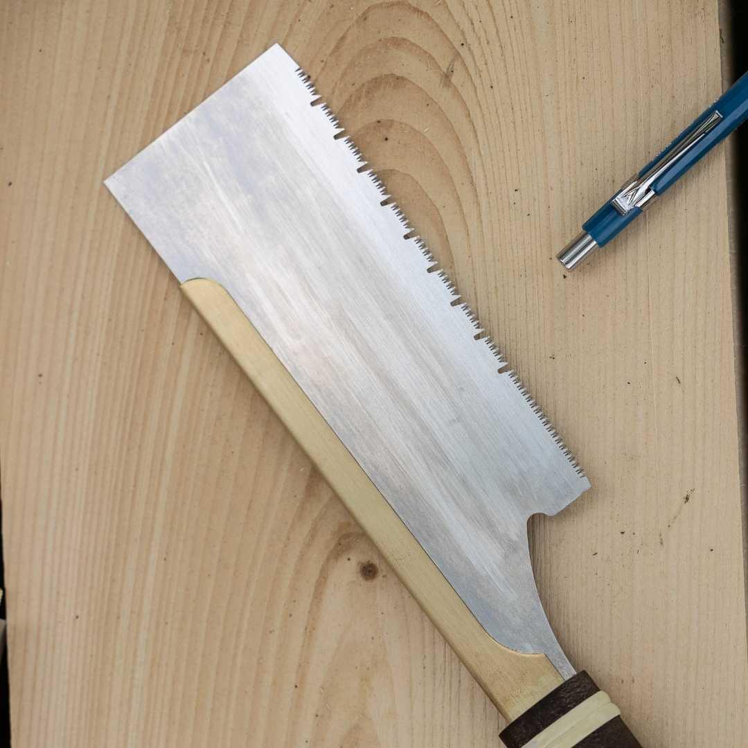 Dozuki pull saw with fine universal cut blade and wooden handle on wood surface, next to a blue pen