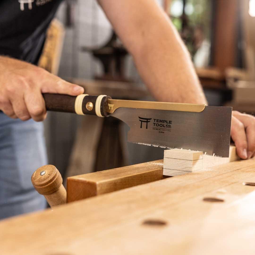 Person using Temple Tool Co. dozuki pull saw with wooden handle to cut small wooden block in woodworking workshop