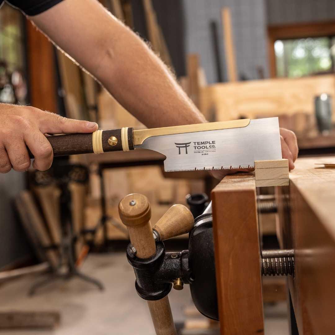 Hands using Temple Tool Co. 150mm Dozuki pull saw cutting a small wood block on a woodworking bench