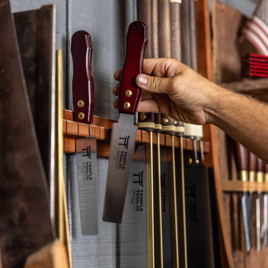 Hand holding Temple Tool Co Flush Cut Pull Saw 150mm with maroon handle in woodworking tool rack