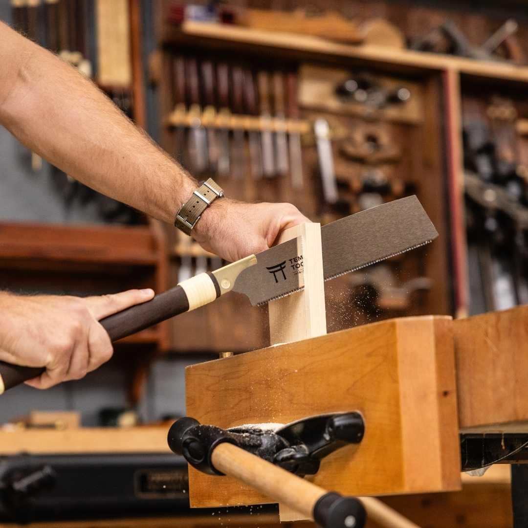 Hands using Temple Tool Kataba pull saw to cut wood in a woodworking shop with tools in background