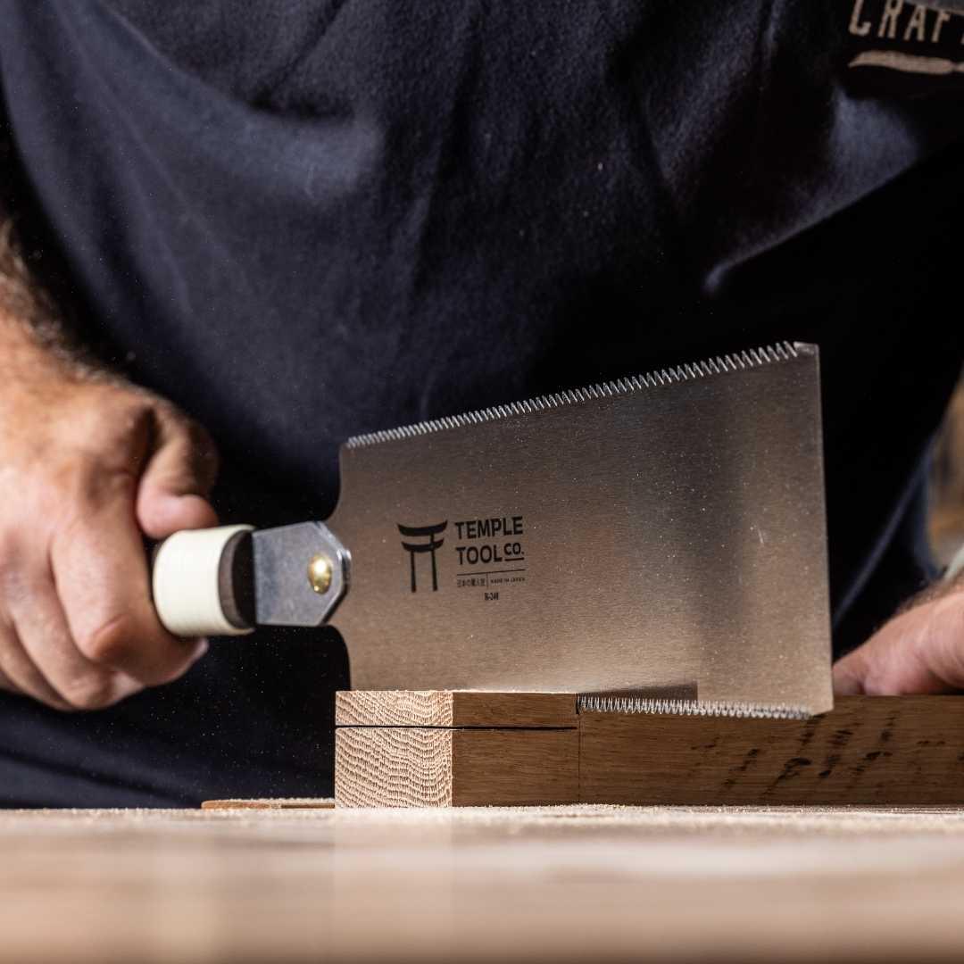 Close-up of hand using Temple Tool Ryoba Japanese saw to cut wooden joints on table