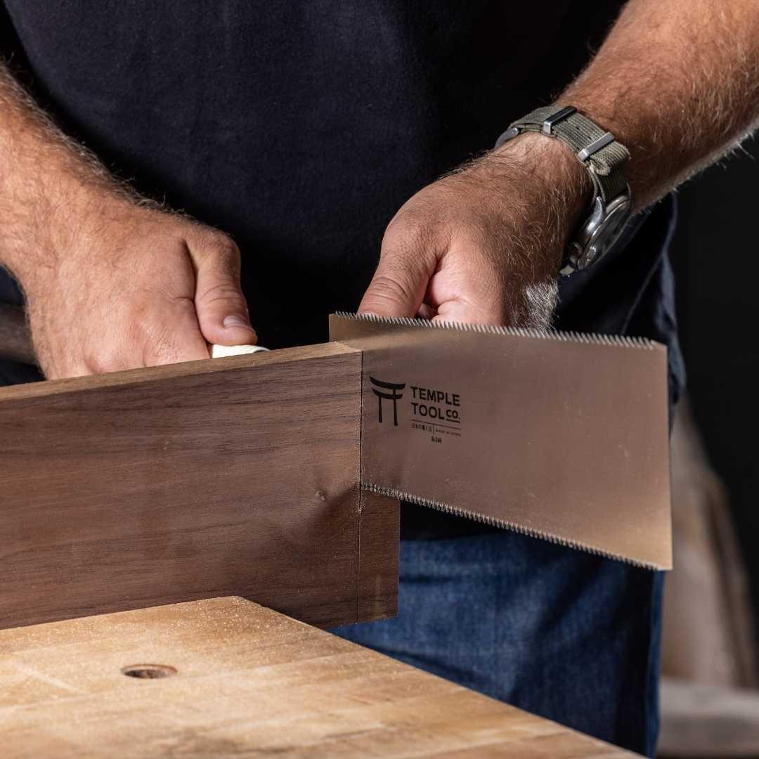 Close-up of hands using a Temple Tool Co Ryoba saw cutting a wooden board on a workbench
