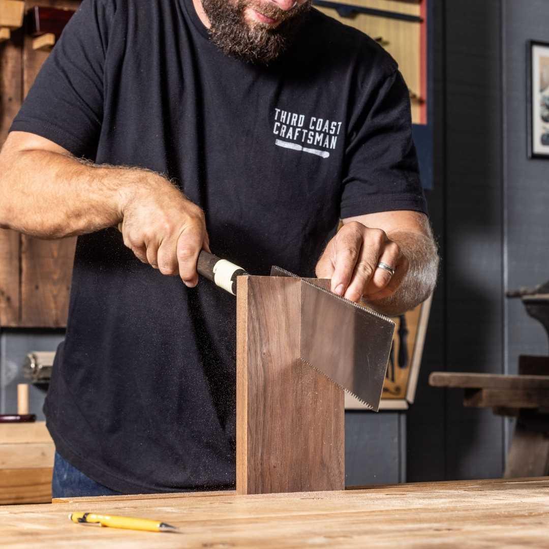 Craftsman using a Temple Tool Ryoba saw to cut a wooden board in a woodworking workshop