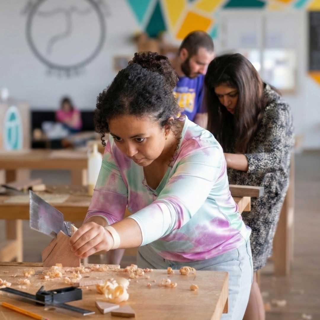 Young girl working on a craft project in a classroom setting with other students in the background.