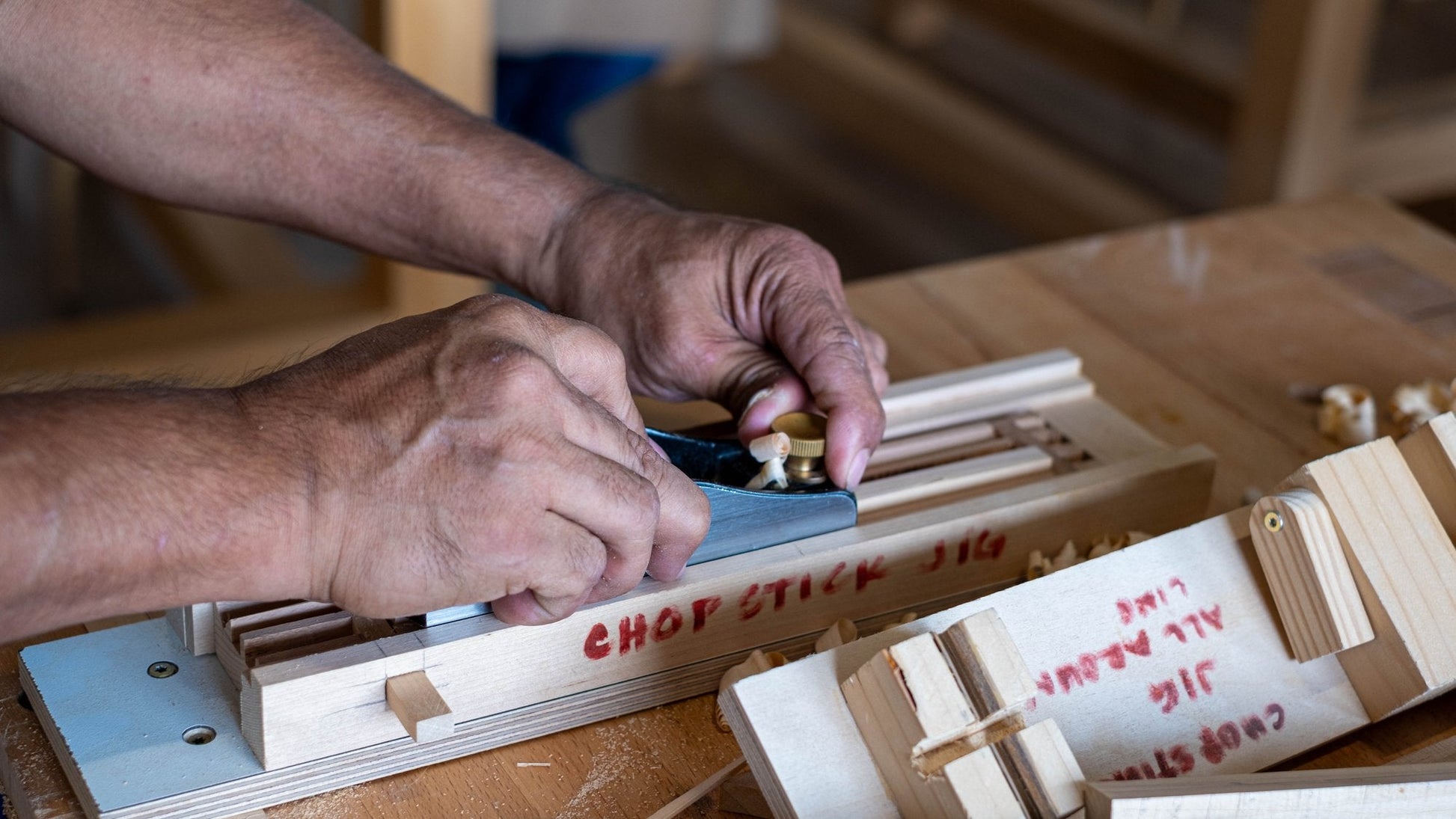 Hands guiding a hand plane along a chopstick blank held in a wooden jig