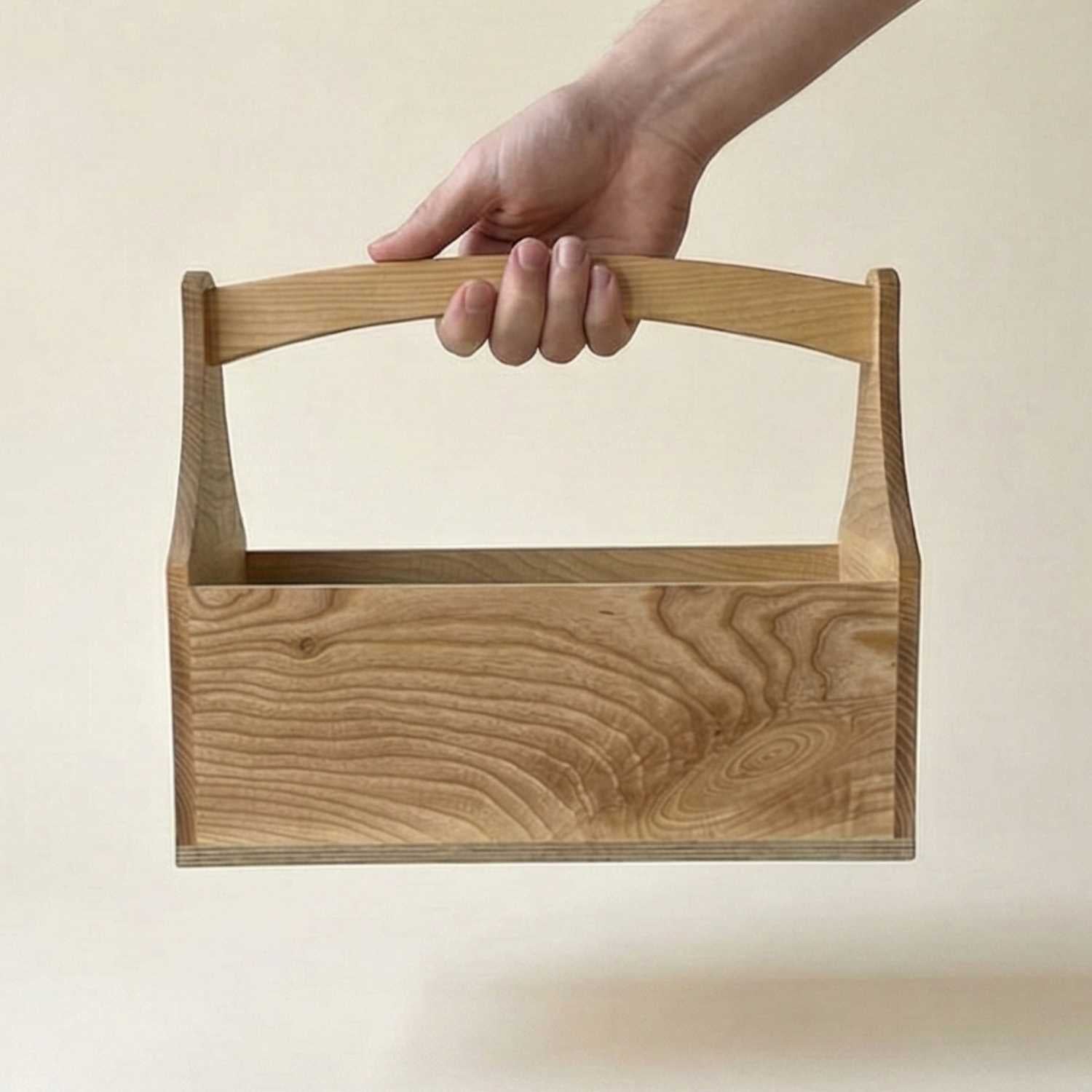 A neutral hand holding the ash wood toolbox made at The Makers Society in Dubai by its curved handle to demonstrate scale, portability, and ergonomic design for woodworking or home storage.