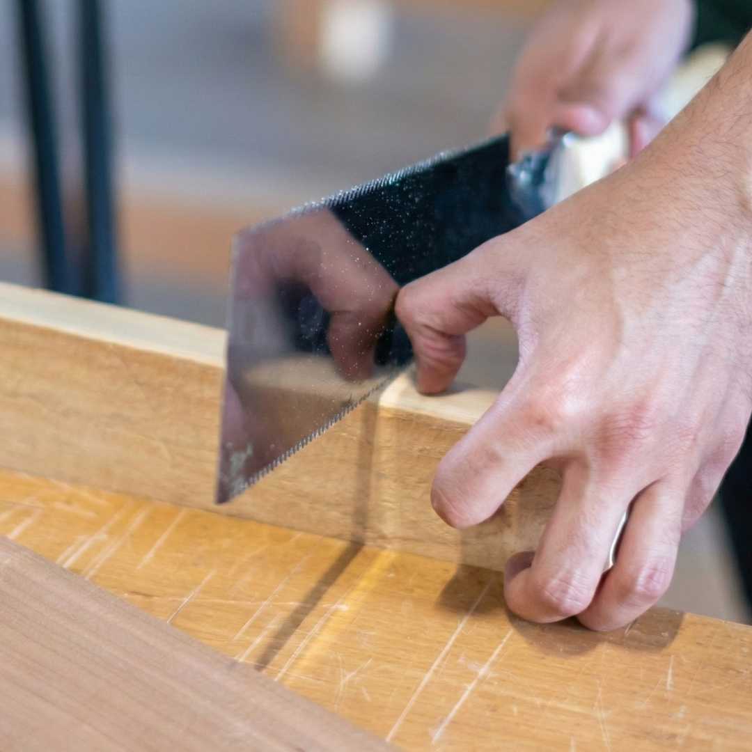 Close-up of hands using a handsaw to cut wood in a woodworking class setting