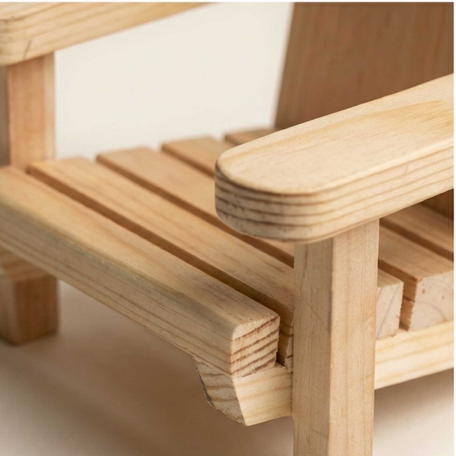 Macro close-up of a miniature wooden chair highlighting the smooth natural grain, rounded armrest finish, and precise joinery of the slatted seat construction.