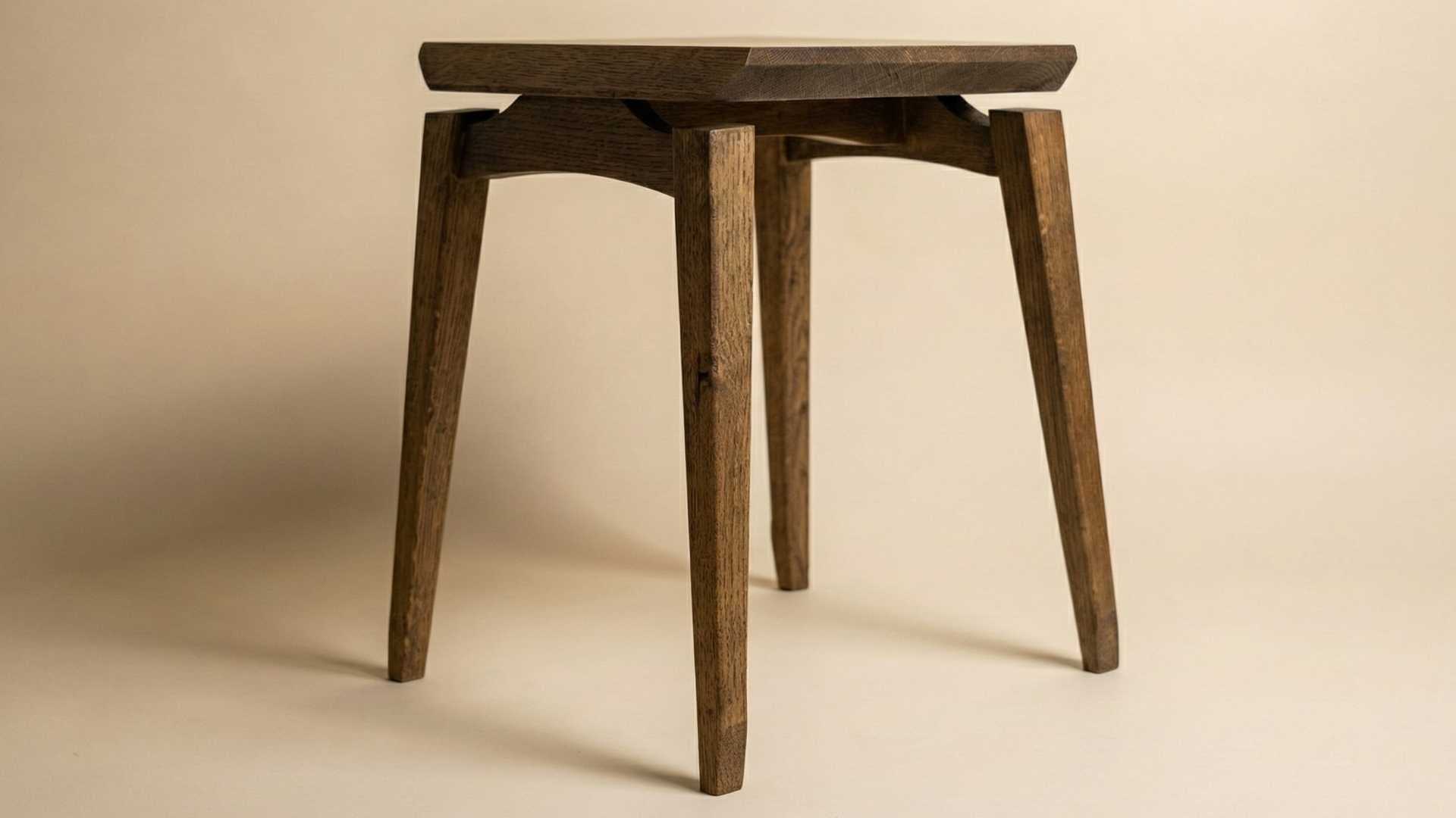 A studio shot of a sleek, dark-stained wooden stool with four tapered legs and a unique floating-seat design.