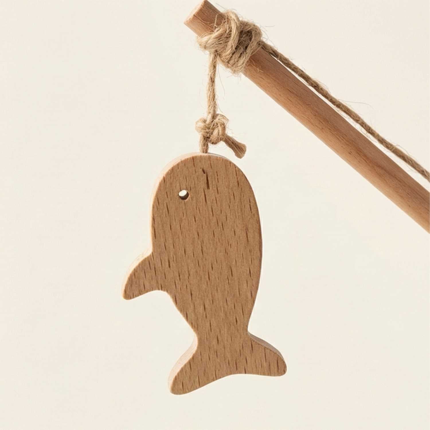 Wooden whale ornament hanging on a stick against a light background