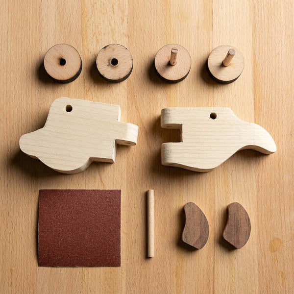 Wooden puppy pull-along kit parts from The Makers Society laid out with wheels, ears, dowel, and sandpaper