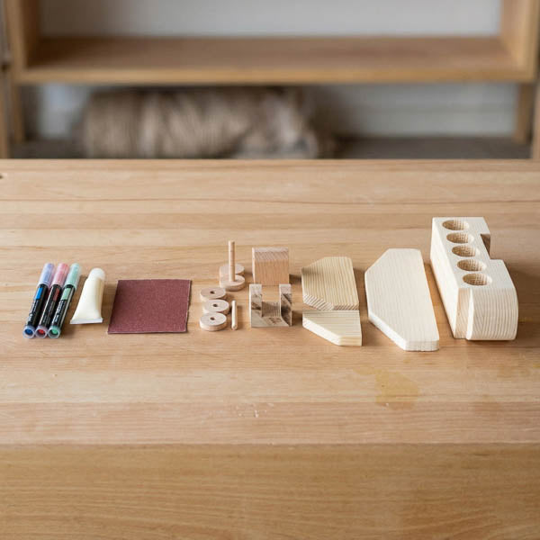 Wooden aeroplane kit contents from The Makers Society laid out with precut pieces, glue, sandpaper, and color markers
