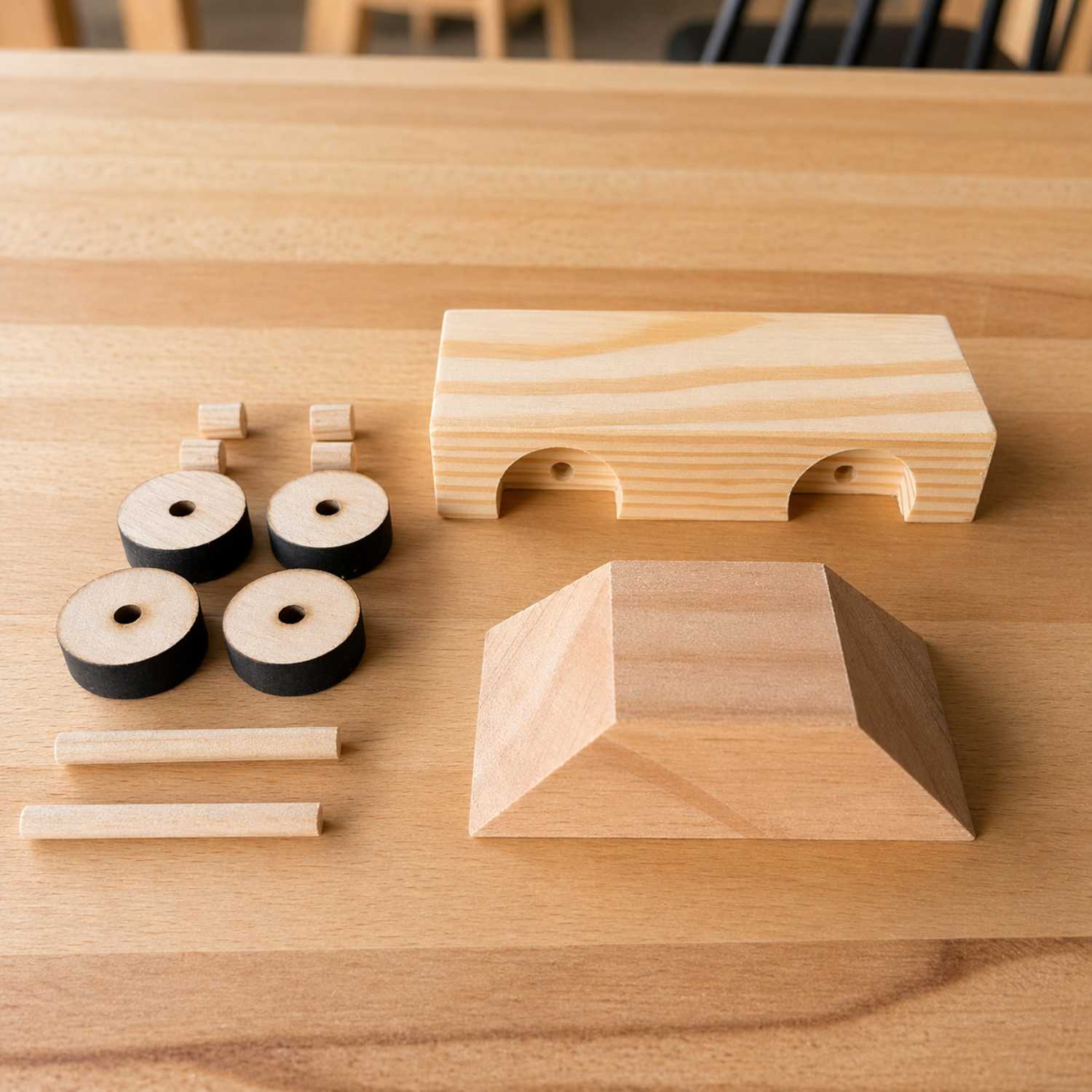 Wooden taxi car kit parts by The Makers Society arranged on a workshop table, including the car body, roof piece, wheels, and wooden axles.