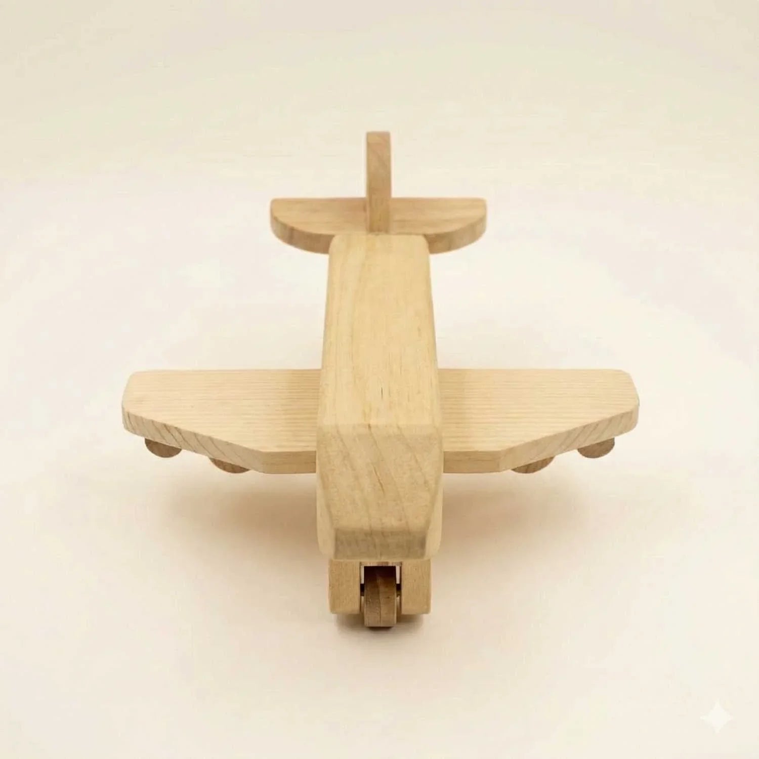 Front-facing view of the wooden toy airplane showing the symmetrical wingspan, nose profile, and the underside landing gear wheels in a minimalist studio setting.
