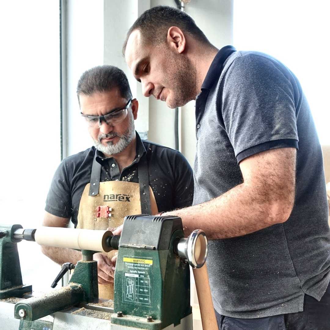 Instructor guiding a student at a wood lathe during a woodturning trial class at The Makers Society in Dubai.