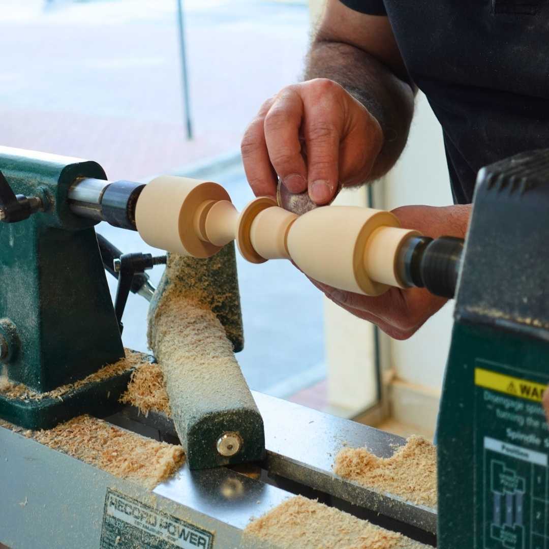 Close-up of hands shaping a spindle on a wood lathe during a woodturning trial class at The Makers Society in Dubai.